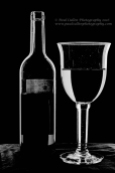 Low key photograph of a wine bottle and glass in high key monochrome.